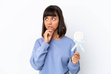 Young mixed race woman holding a lollipop isolated on white background having doubts and thinking