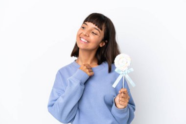 Young mixed race woman holding a lollipop isolated on white background looking up while smiling