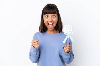 Young mixed race woman holding a lollipop isolated on white background celebrating a victory in winner position