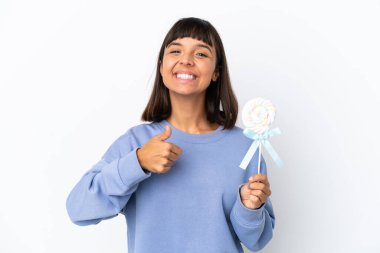 Young mixed race woman holding a lollipop isolated on white background giving a thumbs up gesture