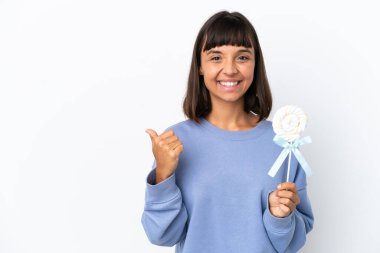 Young mixed race woman holding a lollipop isolated on white background pointing to the side to present a product