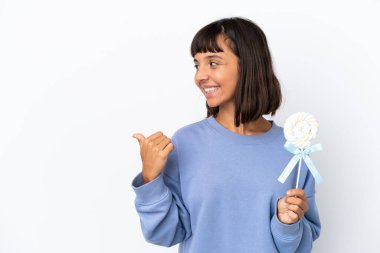 Young mixed race woman holding a lollipop isolated on white background pointing to the side to present a product