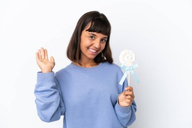 Young mixed race woman holding a lollipop isolated on white background saluting with hand with happy expression