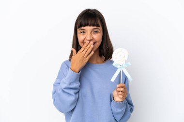 Young mixed race woman holding a lollipop isolated on white background happy and smiling covering mouth with hand