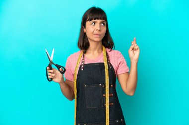 Young mixed race seasmtress woman isolated on blue background with fingers crossing and wishing the best