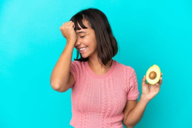 Young mixed race woman holding an avocado isolated on blue background has realized something and intending the solution