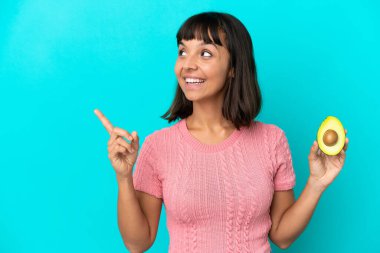Young mixed race woman holding an avocado isolated on blue background intending to realizes the solution while lifting a finger up