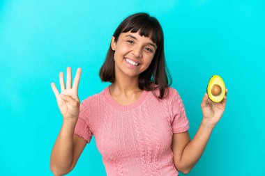 Young mixed race woman holding an avocado isolated on blue background happy and counting four with fingers