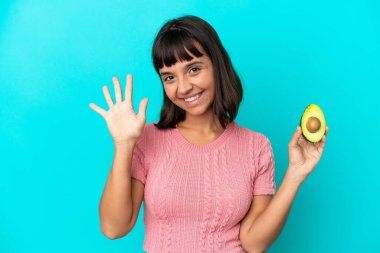 Young mixed race woman holding an avocado isolated on blue background counting five with fingers
