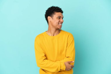 Young African American man isolated on blue background looking to the side and smiling