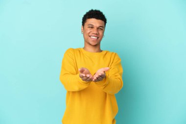 Genç Afrikalı Amerikalı bir adam mavi arka planda izole edilmiş. Bir ilan vermek için fotokopi makinesini avucunun içinde tutuyor.