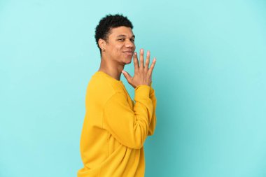 Genç Afrikalı Amerikalı bir adam mavi arka planda bir şeyler planlıyor.