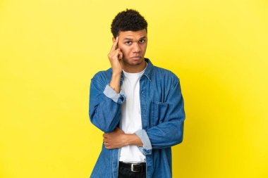 Genç Afrikalı Amerikalı bir adam sarı arka planda izole edilmiş bir fikir düşünüyor.