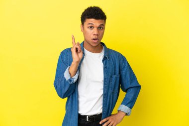 Genç Afrikalı Amerikalı adam sarı arka planda izole edilmiş. Çözümü bulmak için parmağını kaldırıyor.