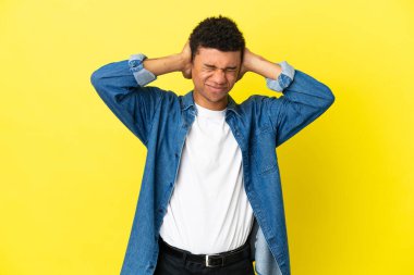 Sarı arka planda izole edilmiş genç Afrikalı Amerikalı hayal kırıklığına uğramış ve kulaklarını kapatmış.