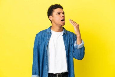 Genç Afro-Amerikalı adam sarı arka planda izole edilmiş esniyor ve ağzı açık bir şekilde elle kapanıyor.