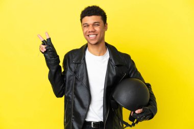 Young African American man with a motorcycle helmet isolated on yellow background smiling and showing victory sign