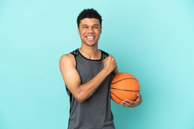 Basketbolcu Afrikalı Amerikalı adam mavi arka planda izole edilmiş zaferi kutluyor.