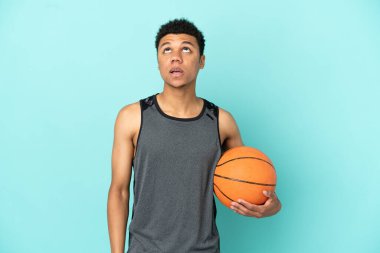 Basketbolcu Afrikalı Amerikalı adam mavi arka planda izole edilmiş yukarı bakıyor ve şaşırmış bir ifadeyle