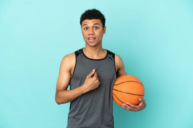 Basketbolcu Afro-Amerikalı adam, mavi arka planda yalıtılmış, şaşırmış yüz ifadesi var.
