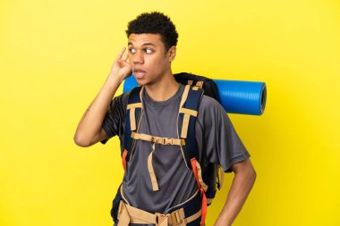 Sarı arka planda izole edilmiş büyük bir sırt çantası olan genç dağcı Afrikalı Amerikalı adam bir şeyler dinlerken elini kulağına koydu.