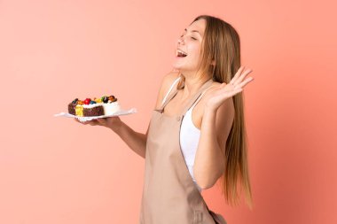 Ukraynalı aşçı pembe arka planda yüzünde sürpriz bir ifadeyle izole edilmiş bir kek tutuyor.