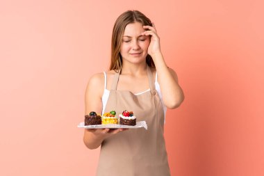 Ukraynalı aşçı pembe arka planda izole edilmiş bir kek tutuyor. Mutsuz ve hayal kırıklığına uğramış bir şekilde. Olumsuz yüz ifadesi