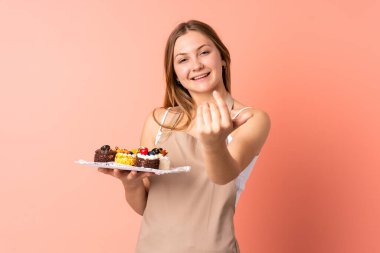 Ukraynalı pasta şefi pembe arka planda izole edilmiş bir kek tutuyor. Gelmeye davet ediyor.