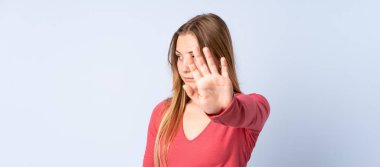 Genç Ukraynalı kız mavi arka planda izole edilmiş. Durma hareketi yapıyor ve hayal kırıklığına uğruyor.