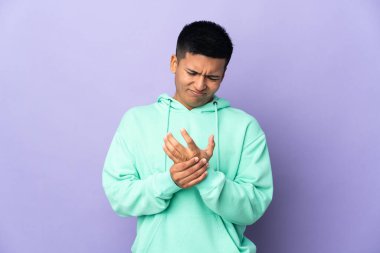 Genç Ekvadorlu, mor arka planda izole edilmiş, ellerinde acıdan muzdarip.