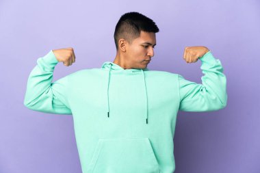 Genç Ekvadorlu, mor arka planda izole edilmiş güçlü bir jest yapıyor.
