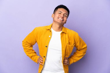 Genç Ekvadorlu adam mor arka planda izole edilmiş, kolları kalçasında ve gülümsüyor.