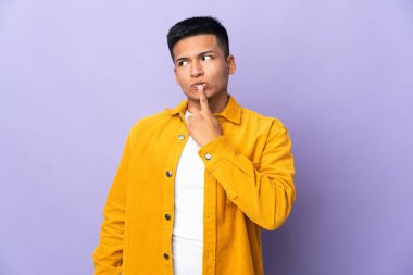 Mor arka planda izole edilmiş genç Ekvadorlu bir adam sessizlik işareti gösteriyor. Parmağını ağzına sokuyor.