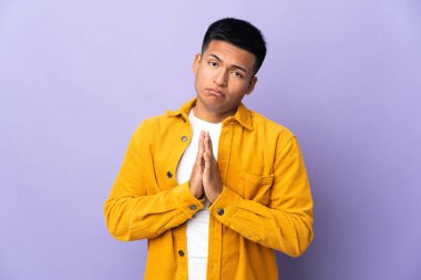 Mor arka planda izole genç Ekvadorlu adam avuç içlerini bir arada tutuyor. İnsan bir şey ister.