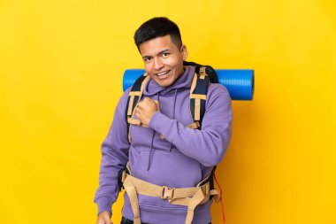 Sarı arka planda büyük bir sırt çantası olan genç dağcı zaferi kutluyor.