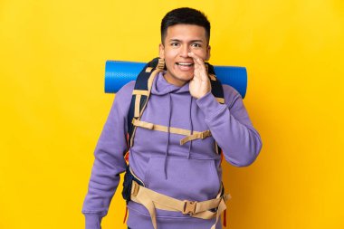 Sarı arka planda izole edilmiş büyük sırt çantalı genç dağcı ağzı açık bağırıyor.