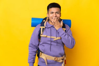 Sarı arka planda izole edilmiş büyük sırt çantalı genç dağcı adam mutlu ve gülümsüyor.