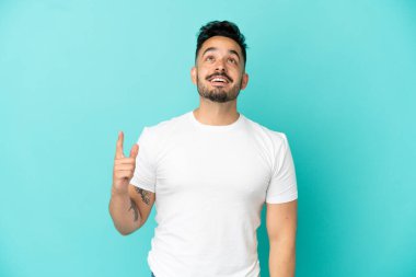 Mavi arka planda izole edilmiş genç beyaz adam yukarı bakıyor ve şaşırıyor.