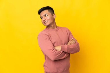 Sarı arka planda izole edilmiş, kolları çapraz ve mutlu genç Ekvadorlu adam.
