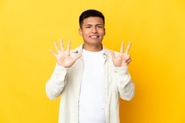 Sarı arka planda izole edilmiş genç Ekvadorlu sekiz parmaklı sayıyor.