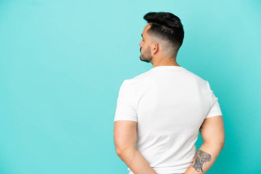 Kafkasyalı genç adam mavi arka planda izole edilmiş ve arkasına bakıyor.