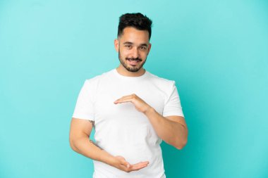 Mavi arka planda izole edilmiş genç beyaz adam bir ilan vermek için avucunun içinde hayali bir fotokopi makinesi tutuyor.