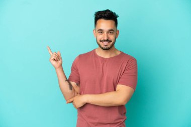 Mavi arka planda izole edilmiş genç beyaz adam mutlu ve dik duruyor.