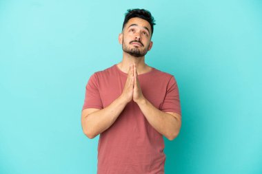 Mavi arka planda izole edilmiş genç beyaz adam avuç içlerini bir arada tutuyor. İnsan bir şey ister.