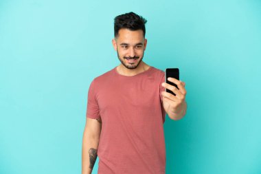 Mavi arka planda izole edilmiş genç beyaz bir adam selfie çekiyor.