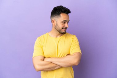 Mor arka planda izole edilmiş genç beyaz adam yana bakıyor ve gülümsüyor.