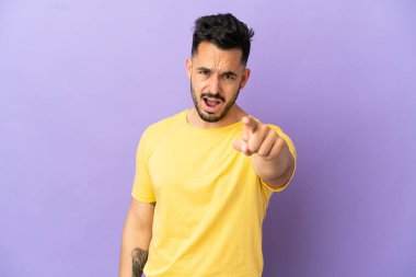 Mor arka planda izole edilmiş genç beyaz adam hayal kırıklığına uğramış ve ön tarafı işaret ediyor.