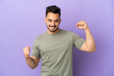 Mor arka planda izole edilmiş genç beyaz bir adam zaferi kutluyor.