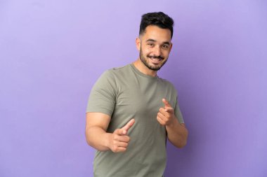 Mor arka planda izole edilmiş genç beyaz adam öne bakıyor ve gülümsüyor.