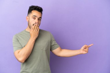 Mor arka planda izole edilmiş beyaz bir genç, sürpriz bir ifadeyle işaret ederken